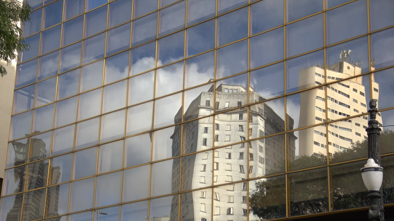 Reflections of city buildings on a glass facade creating a mirrored urban landscape.