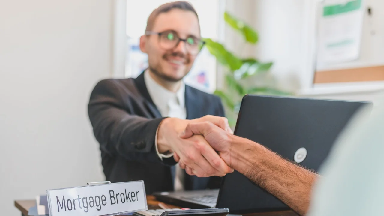 Mortgage broker and client sealing a deal with a handshake in a bright, modern office.