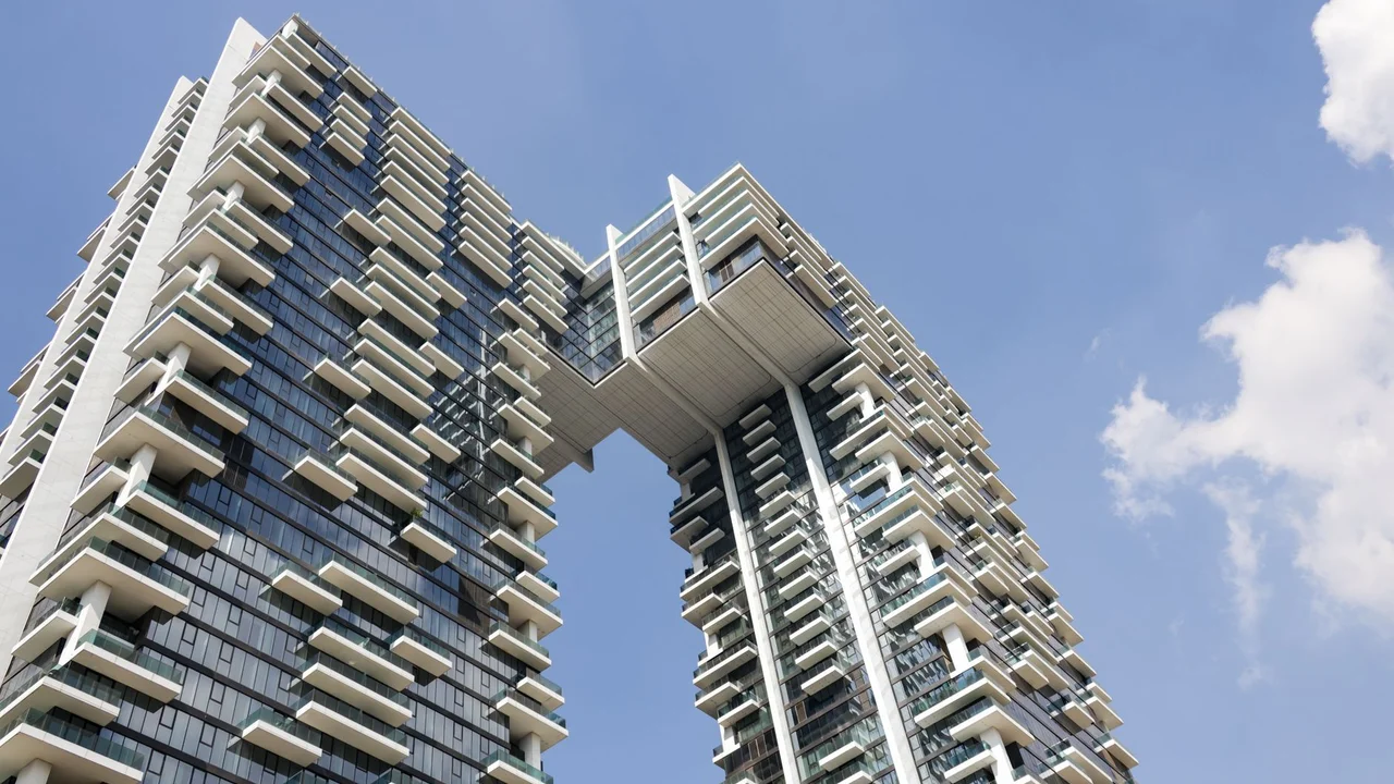 Contemporary high-rise building with a distinctive bridge design against a clear sky.