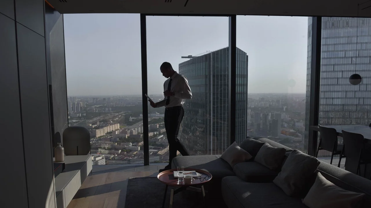 Silhouette of a businessman standing in a luxury apartment with a panoramic cityscape view.