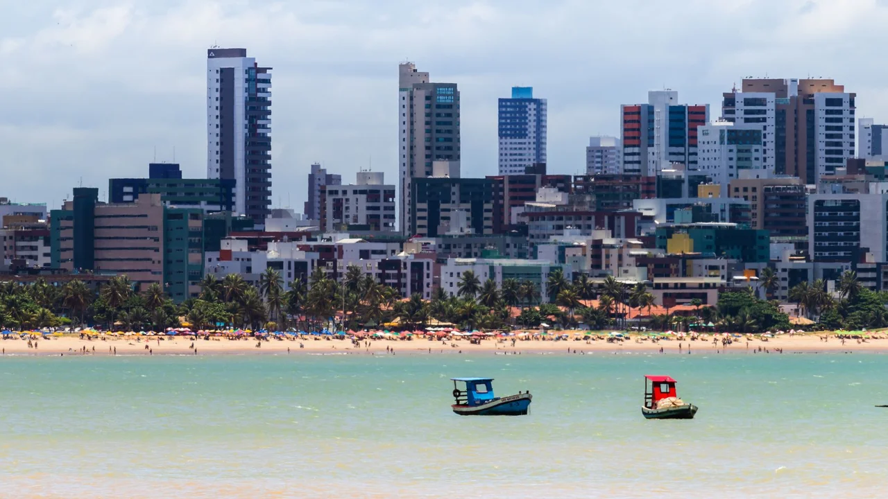 Skyline of João Pessoa's beachfront with boats in the foreground on a sunny day.