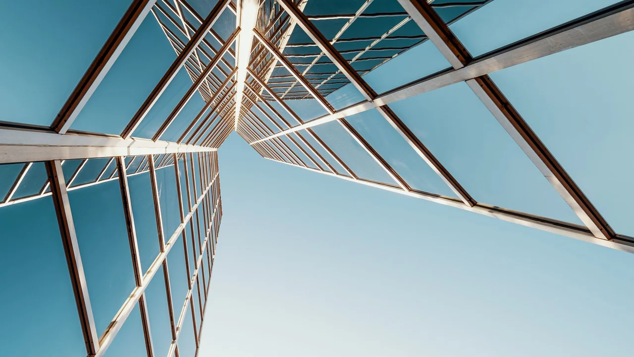 From below of multistory geometric building with glass mirrored windows reflecting cloudless blue sky on sunny day