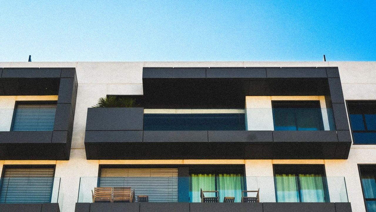 Minimalist apartment facade with glass balconies against a clear blue sky.