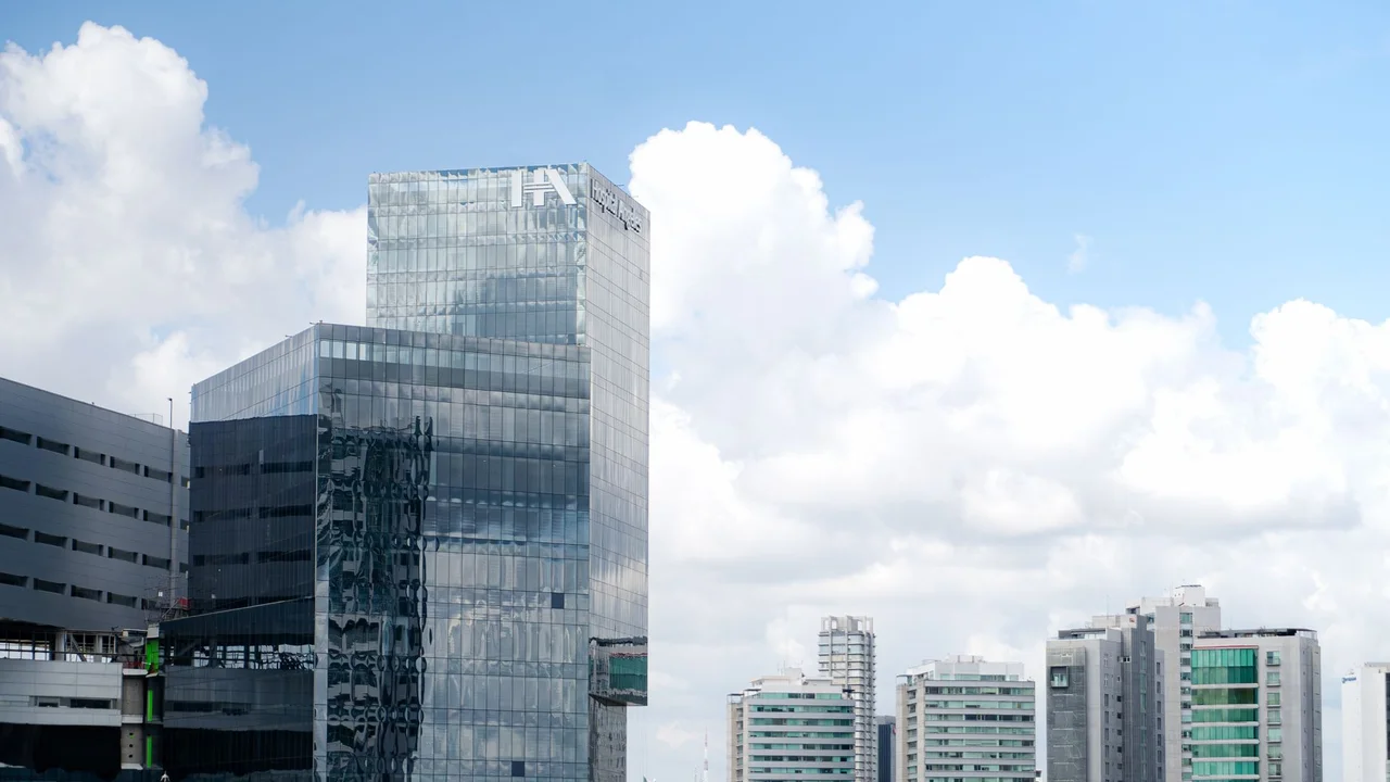Panoramic view of sleek, glass skyscrapers with blue sky and clouds.