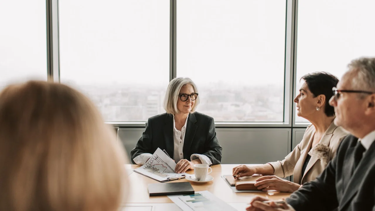 A group of professionals engaged in a business meeting inside a modern office boardroom.