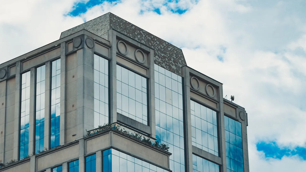 Low angle of contemporary geometric building with glass mirrored windows reflecting cloudy blue sky