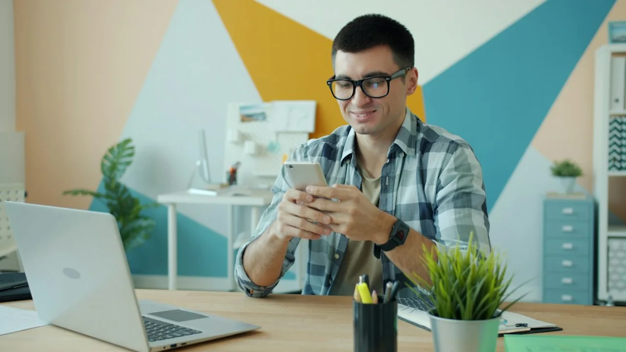 Man in glasses using phone at office desk