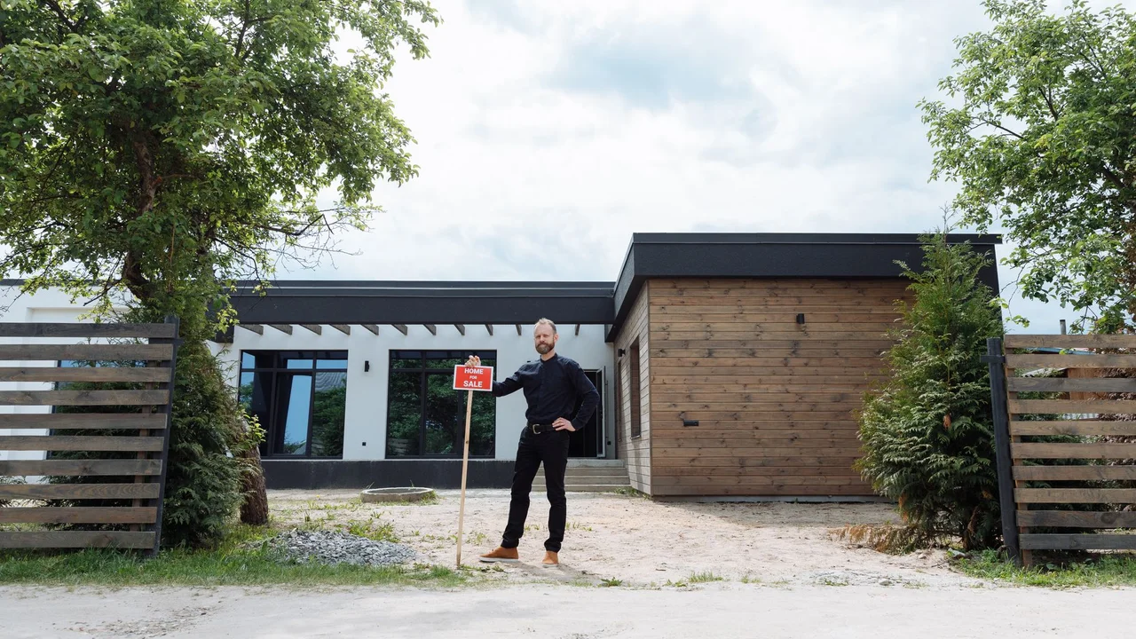 Real estate agent standing outside modern house with for sale sign, featuring contemporary design.