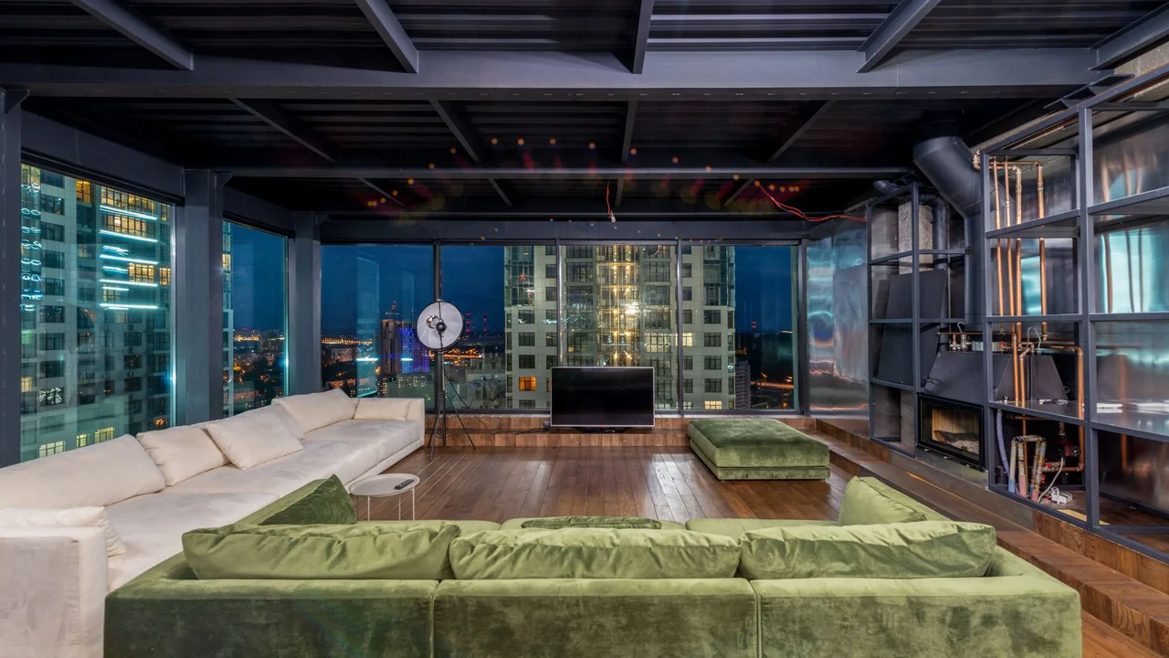 Interior of contemporary spacious living room with large comfortable sofas and panoramic windows in evening time